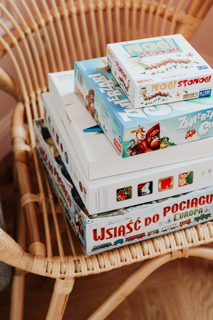 Close-up of various board games stacked on a woven rattan chair indoors.